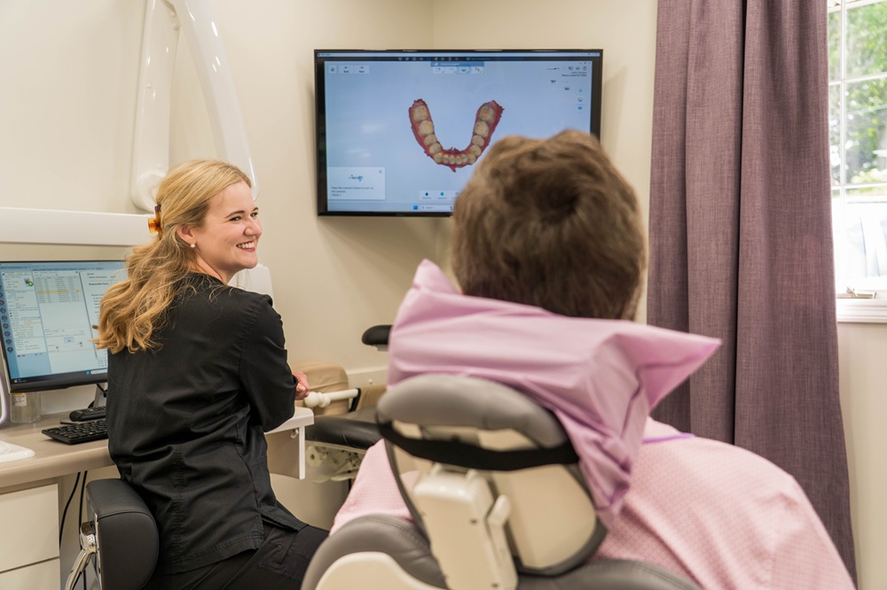 Dr. Erika Lovett, DMD, smiling while showing a dental scan on a large screen to a patient seated in the chair during a consultation in a modern dental operatory – Kingsport Dentist