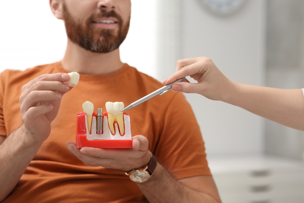 A man holds a dental model while a dentist explains the implant process, highlighting personalized treatment and patient education – Dental Implants Kingsport, TN.