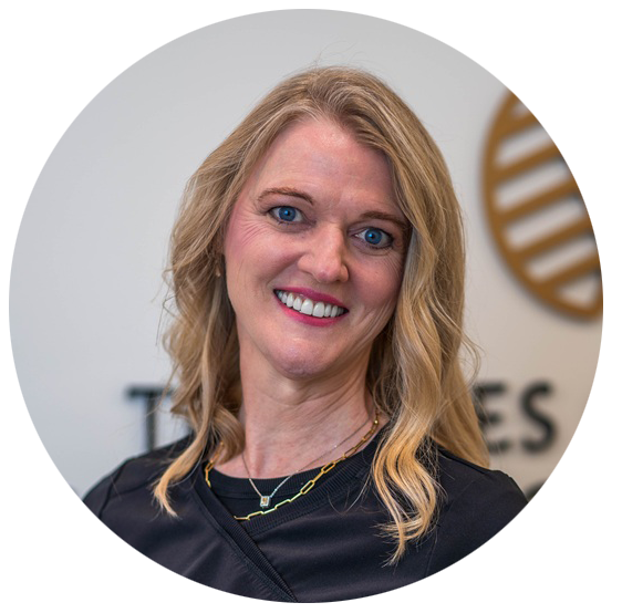 Dr. Kathy Sanders, DMD, FAACD, smiling in a professional headshot wearing a black dental uniform with the Tri-Cities Center for Cosmetic Dentistry logo blurred in the background – Kingsport Dentist