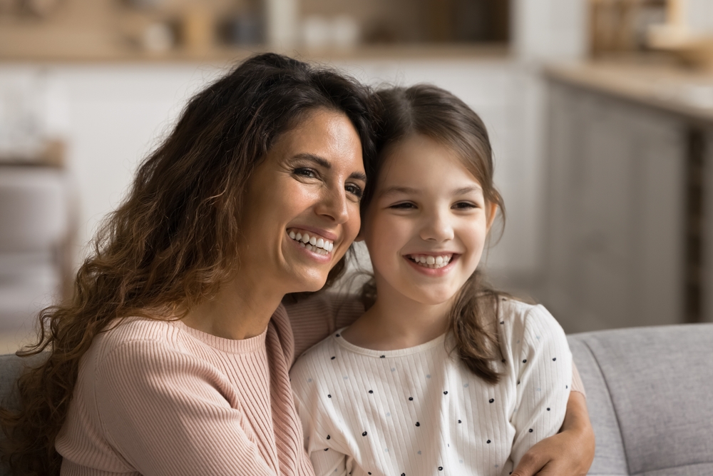 Mother and Daughter with Bright Smiles - Porcelain Crowns and Bridges A joyful mother and daughter share a warm hug, showcasing healthy, beautiful smiles made possible by advanced porcelain crowns and bridges.