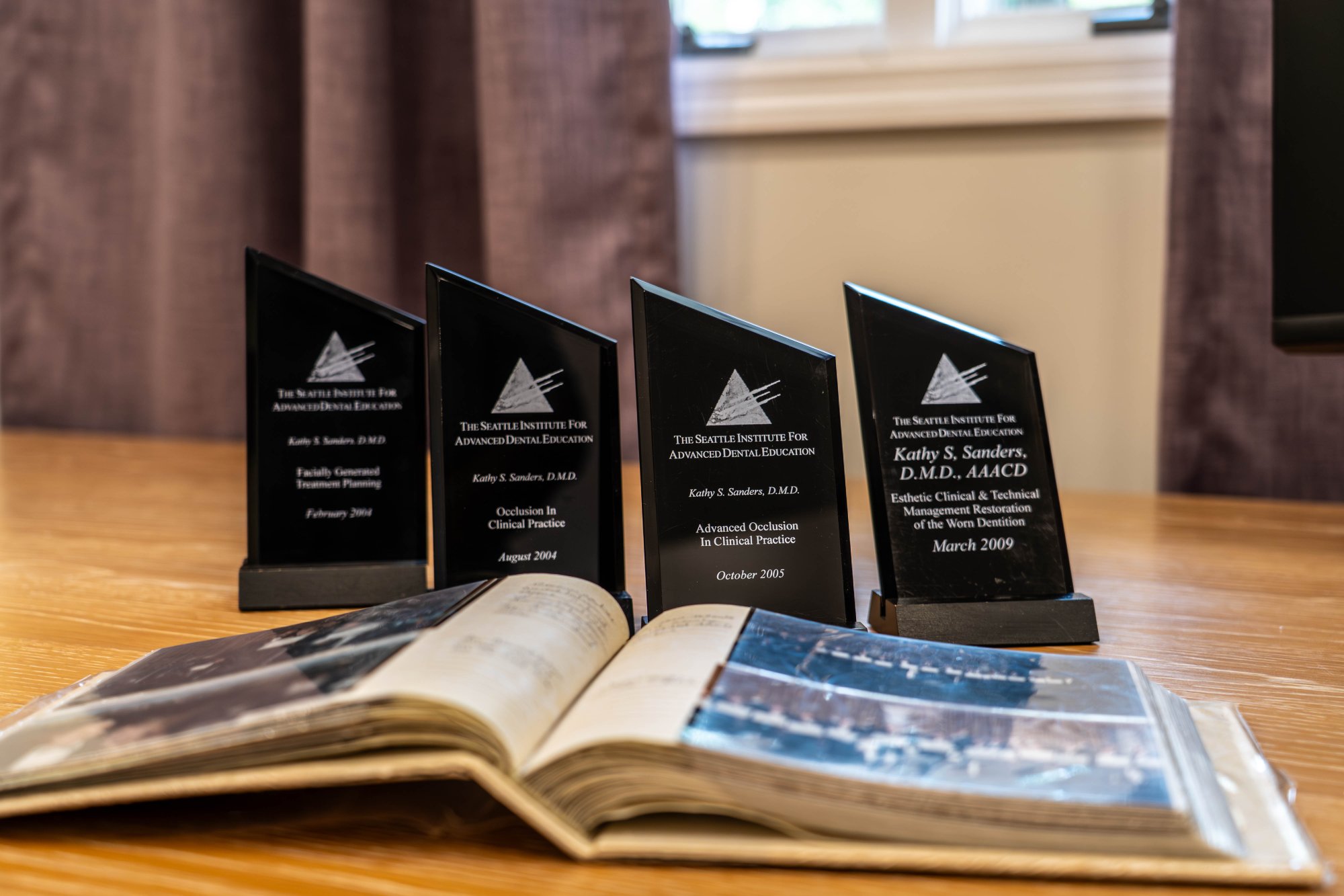 Award Recognition Reflecting Our Dental Clinic Mission Statement Four dental awards displayed behind an open photo album on a wooden table, symbolizing a commitment to excellence and patient-centered care—dental clinic mission statement