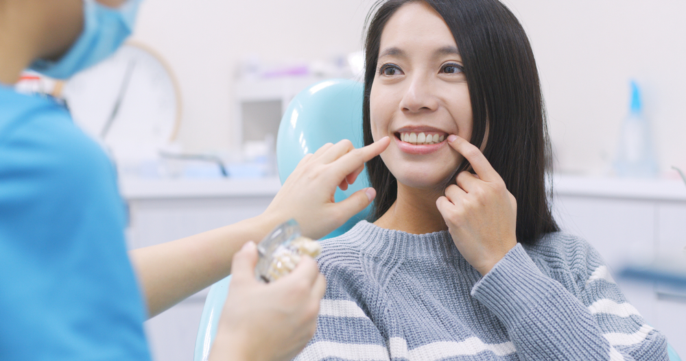 Dentist Consultation for Smile Enhancement – Porcelain Veneers A woman in a dental chair smiles and points to her teeth while discussing treatment options, representing the transformative benefits of porcelain veneers.