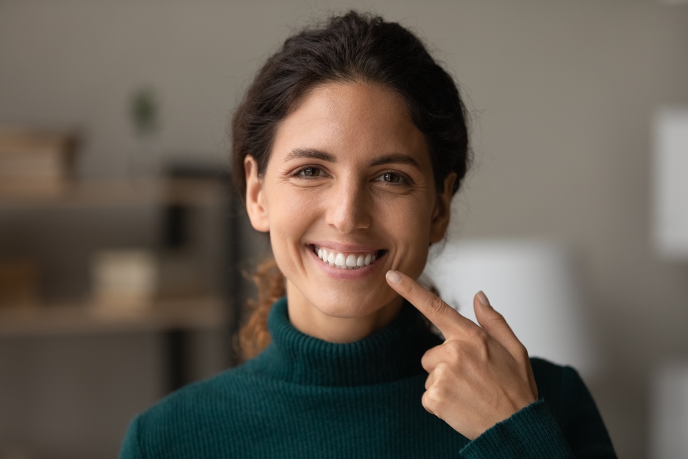 Confident Woman Showing Her Restored Smile - Implant-Supported Crowns and Bridges A smiling woman proudly points to her teeth, representing the confidence and functionality restored through implant-supported crowns and bridges.